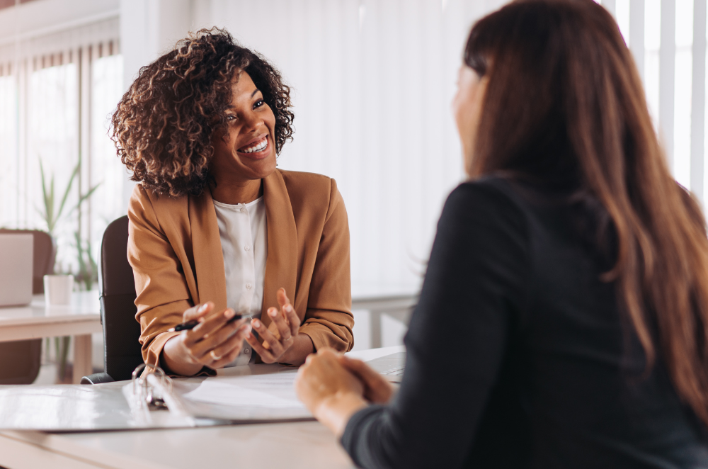 a woman that owns a business looking at her employee and smiling while talking about group benefits.